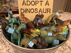 there are many toy dinosaurs in the bowl on the table with a sign that says adopt a dinosaur