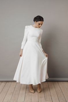 a woman in a white dress standing on a wooden floor with her hands behind her back