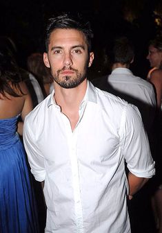 a man in a white shirt standing next to other people at a party and posing for the camera