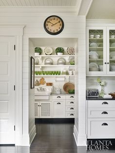 a clock mounted to the side of a wall above a kitchen counter with dishes on it