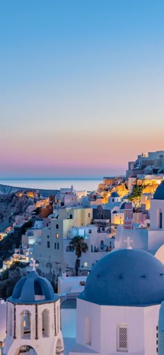 the sunset is shining over some white buildings with blue domes in front of water and city lights