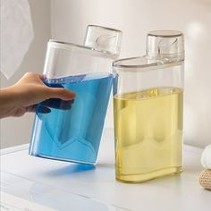 a person is holding a container with blue liquid and yellow liquid next to each other