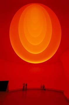 two people standing in front of a red wall with an orange ball on it's ceiling