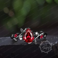 a ring with a red stone surrounded by leaves and vines on top of a black surface