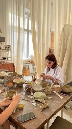 two women sitting at a table making bowls and spoons with pottery on the table