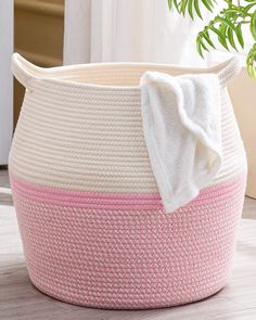 a pink and white basket sitting on top of a wooden floor next to a potted plant