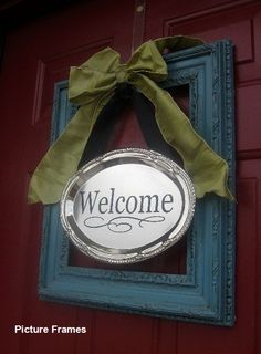 a welcome sign hanging from the side of a red door with a green bow on it