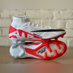 a pair of white and red soccer cleats sitting on top of a wooden table