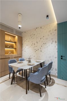 a dining room table with blue chairs in front of a wallpapered wall and shelves