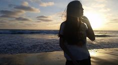 a woman standing on top of a sandy beach next to the ocean at sun set