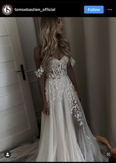 a woman standing in front of a mirror wearing a wedding dress with white flowers on it