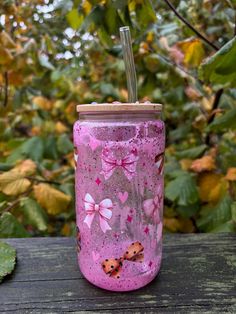 a pink tumbler sitting on top of a wooden table next to leaves and trees