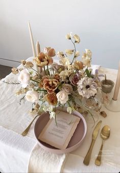 an arrangement of flowers in a vase on a table with silverware and napkins