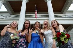 four girls in dresses posing for the camera with their fingers up and one girl holding an american flag