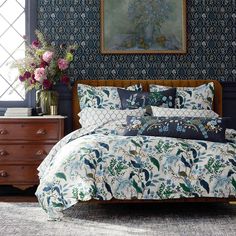 a bed in a room with blue wallpaper and floral designs on the walls, along with a wooden dresser