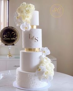 a three tiered wedding cake with white flowers on the top and gold trimmings