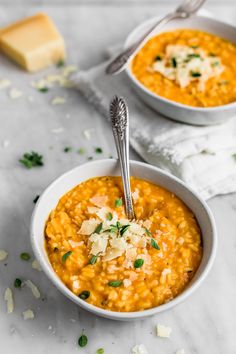 two bowls of red lentula soup with parmesan cheese on top and bread in the background