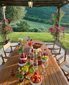 a wooden table topped with bowls of fruit next to a lush green hillside covered in flowers