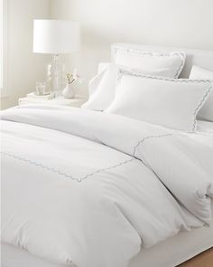 a bed with white sheets and blue scalloped trim on the pillowcases