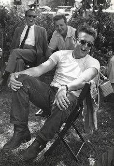 a black and white photo of people sitting in lawn chairs with one man wearing sunglasses