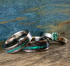 two wedding rings with green and blue opal inlays are sitting on a wooden surface