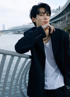 a young man leaning on a metal bench next to the water with his hand under his chin