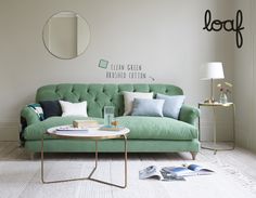 a living room with a green couch and coffee table in front of a mirror on the wall