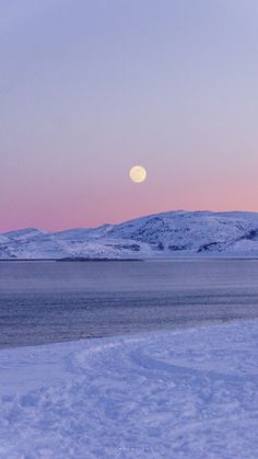 the moon is setting over an icy lake with mountains in the backgrouds