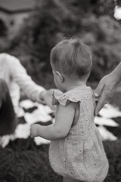 a woman is holding the hand of a baby who is standing in front of her