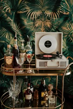 an old record player sitting on top of a bar cart filled with bottles and glasses