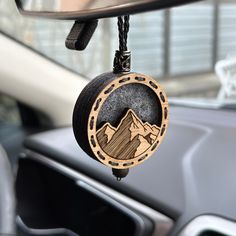 a car dashboard with a wooden badge hanging from it's side window and mountains in the background