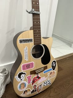 a wooden guitar with stickers on it sitting on the floor next to a pair of shoes