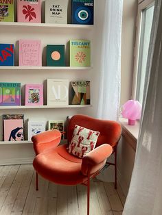 an orange chair sitting in front of a window next to a book shelf filled with books