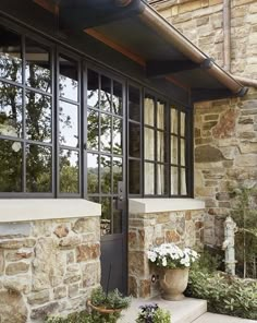 a stone house with large windows and potted plants