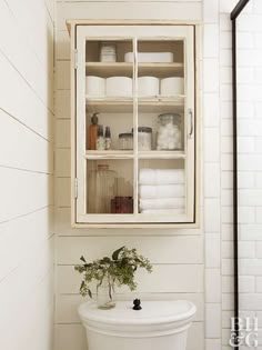 a white toilet sitting in a bathroom next to a cabinet filled with bottles and jars