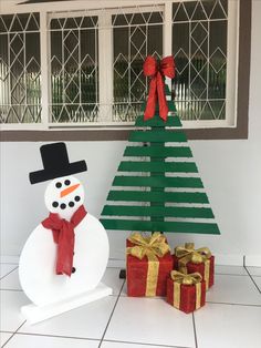 a snowman next to a christmas tree made out of cardboard and wrapped with ribbon