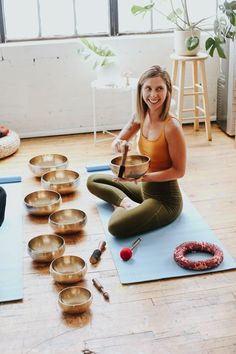 a woman sitting on a yoga mat in front of many singing bowls with one hand