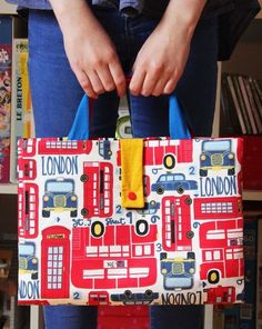 a woman holding a red and blue bag with london on it's front pocket