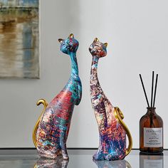 two colorful cats sitting on top of a table next to a bottle and reed diffuser