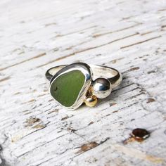 This cluster ring is truly unique. It consists of a bezel set green piece of sea glass, a silver pebble and solid 9ct gold blob. The ring band is a uk size n and a half and the ring is 3mm in width. The sea glass is 12 x 8mm at its widest points and the silver pebble is 4mm in diameter. The ring has a beautiful polished finish and comes presented in a gift box making a perfect gift. It's in stock and will be dispatched within 1-3 working days via Royal Mail Recorded. Silver Handmade Ring, Handmade Green Rings With Recycled Glass, Sea Pottery Jewelry, Sea Glass Rings, Silversmithing Jewelry, Pebble Ring, Sea Glass Ring, Silver Rings With Stones, Bezel Set Ring