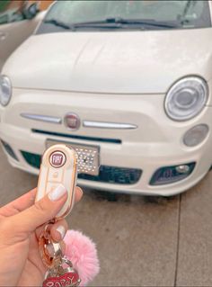 a person is holding a car key in front of a white fiat parked on the street