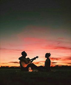 two people sitting in the grass playing guitar at night with an orange and pink sky behind them