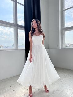 a woman in a white dress standing by a window