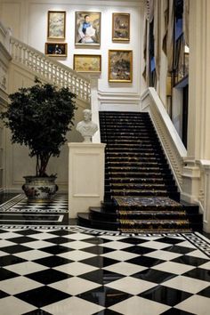 an elegant staircase with black and white tiles on the floor next to a potted plant