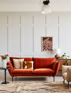 a living room with an orange couch and two chairs in front of a white paneled wall