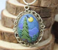 a necklace with an image of trees and the moon on it is sitting on top of a tree stump