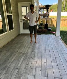 a man standing on a porch next to a white house with wood floors and doors