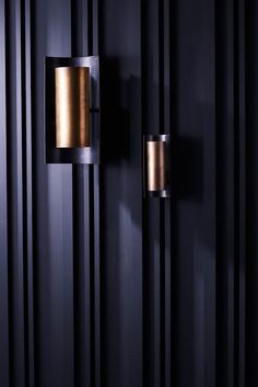 two black and gold wall lights on the side of a dark colored room with vertical striped walls