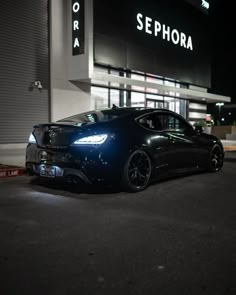 a black sports car parked in front of a building at night with its lights on