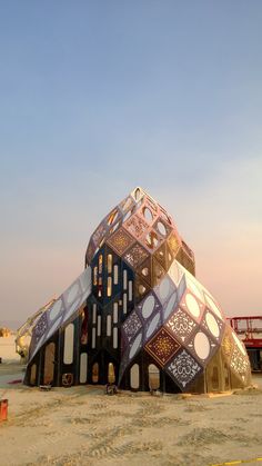 a large building made out of different types of tiles on the beach with people standing around it